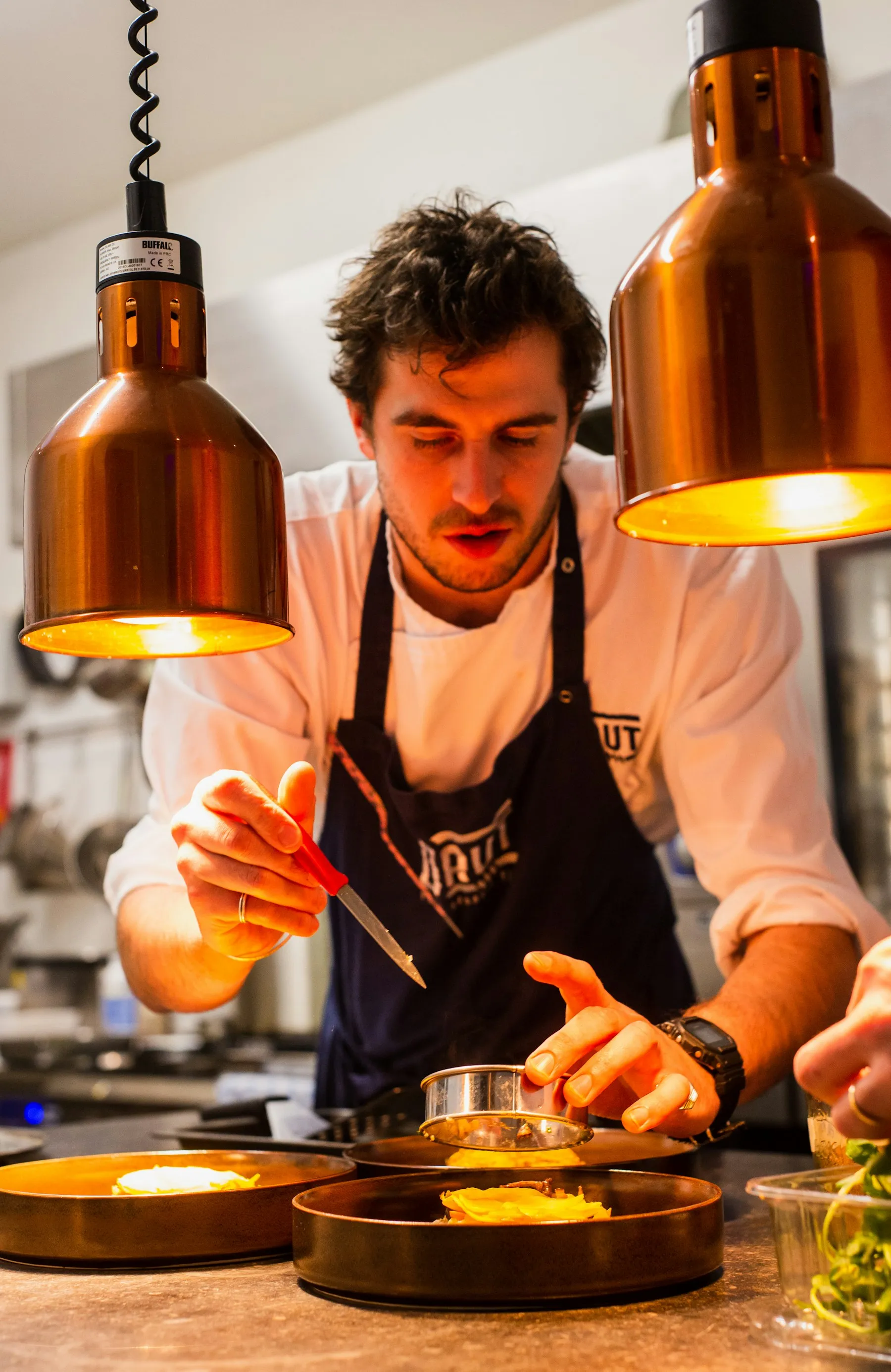 Chef dressant une assiette sous les lampes chauffantes de sa cuisine